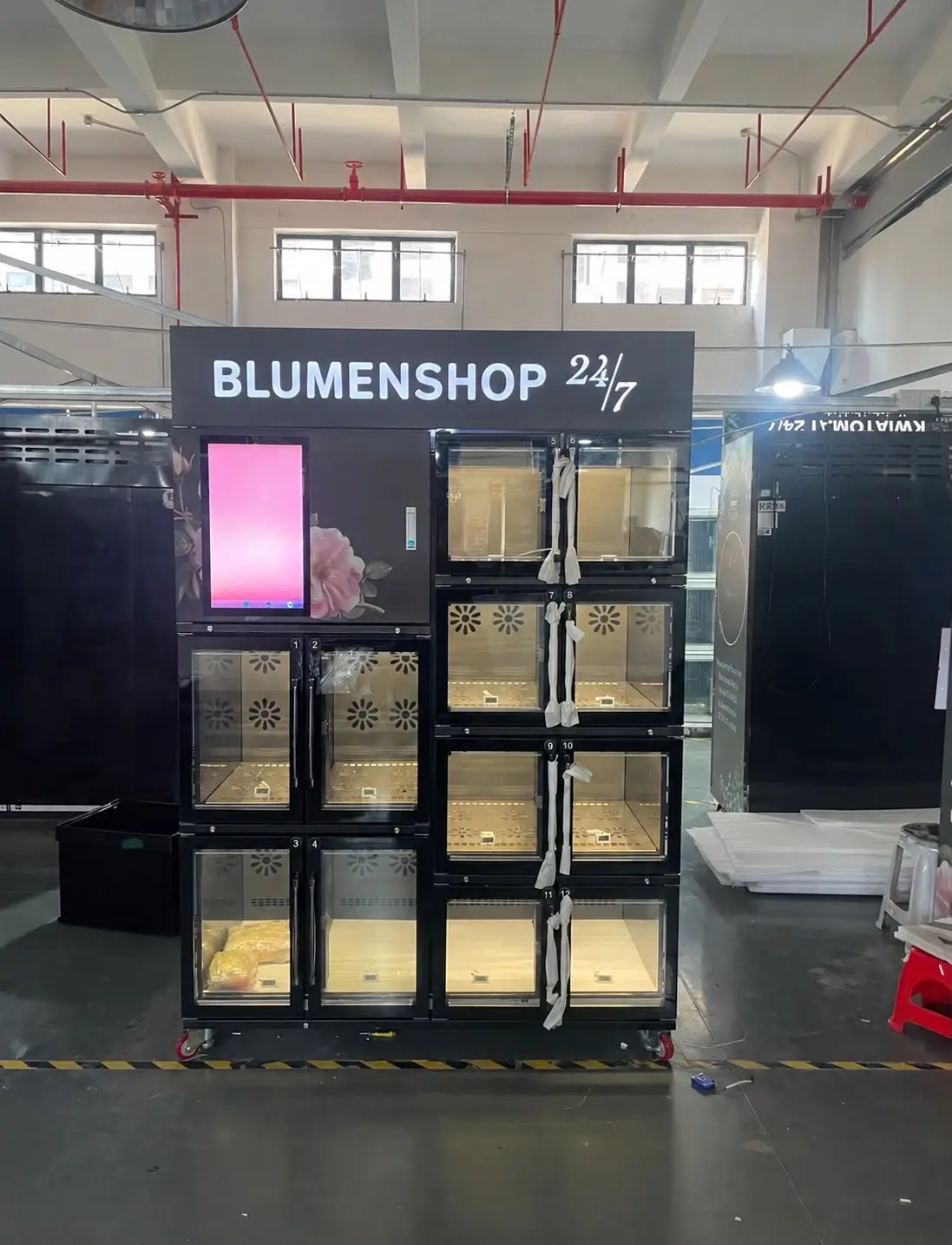 An installed twelve-compartment machine in black; the illuminated fascia carries the customer’s lettering.