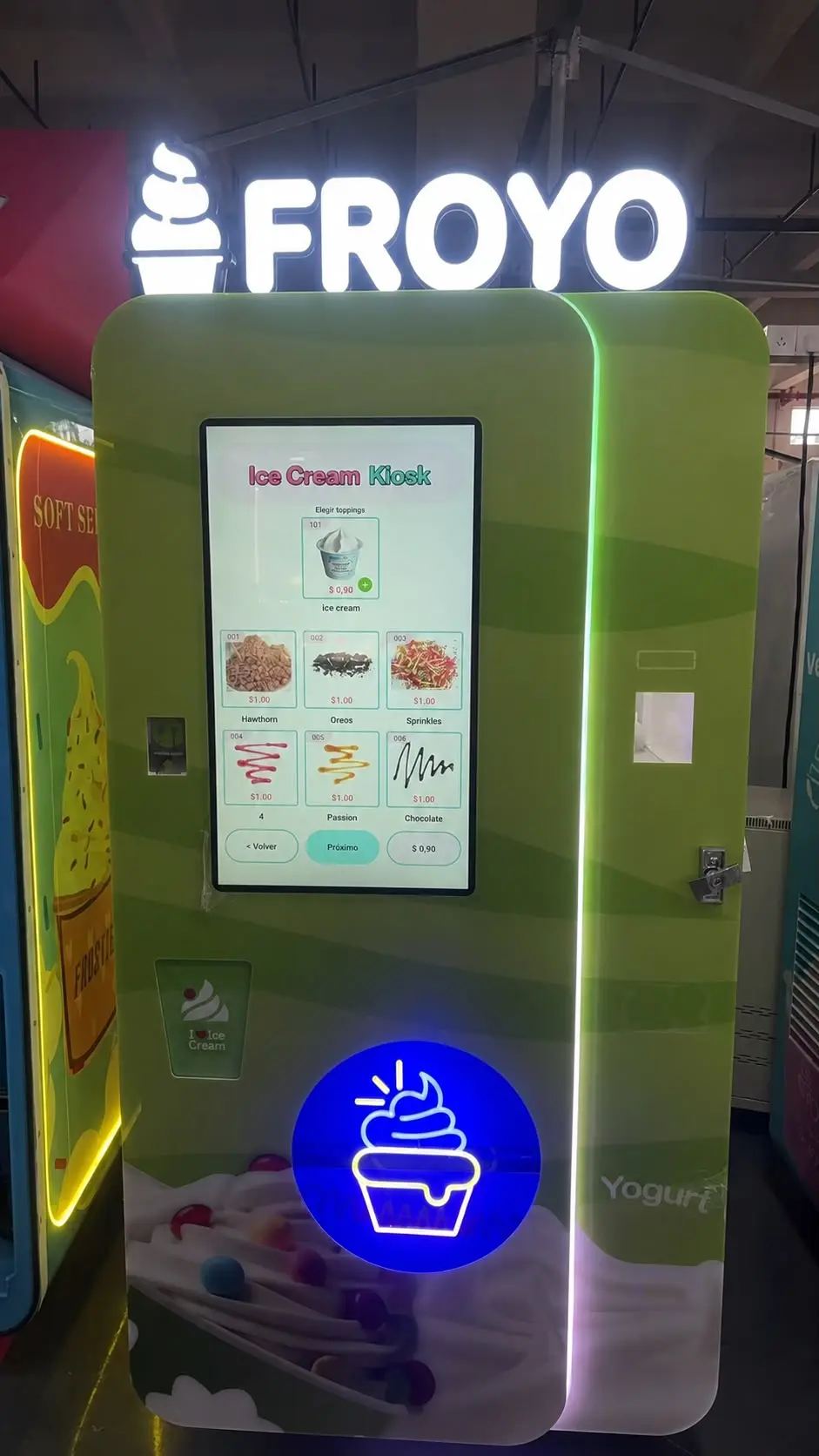 A machine of the same model, the whole unit: green cabinet with a portrait touchscreen, the customer’s illuminated lettering above it and the cup dispenser in front.
