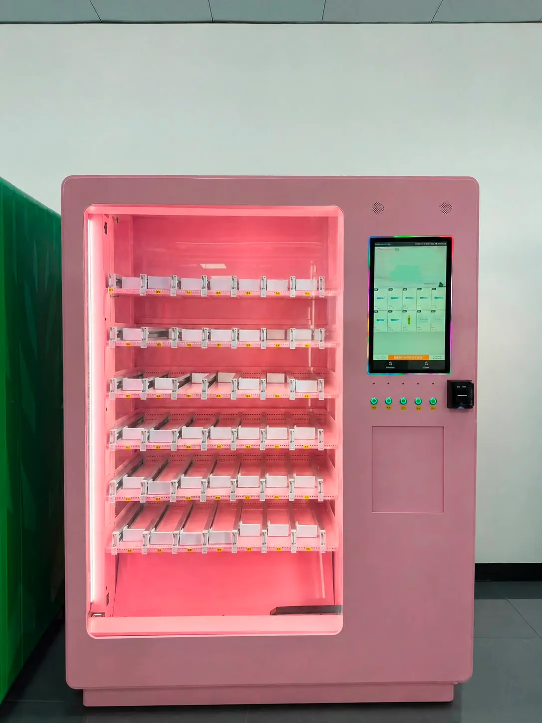 A machine of the same model, the whole unit: pink cabinet, sliding channels on several levels behind lit glass, with touchscreen and card reader beside it. The lanes are still empty.
