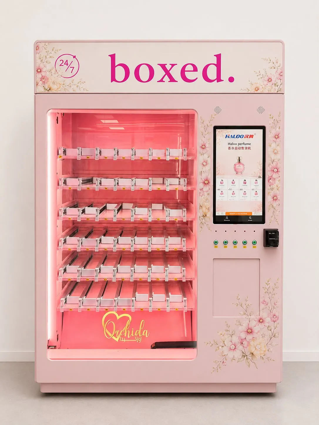 boxed. Parfümautomat in Rosé mit Blumendekor auf der Front, sechs Ebenen Gleitkanäle hinter beleuchtetem Glas und hochformatigem Touchscreen daneben.